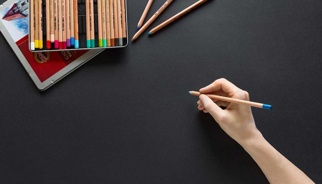 Black surface, hand with colored pencil waiting to draw or write something