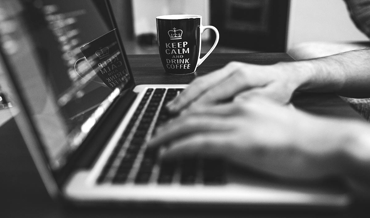 hands on computer keyboard, cup with text "Keep calm - drink coffee" in background