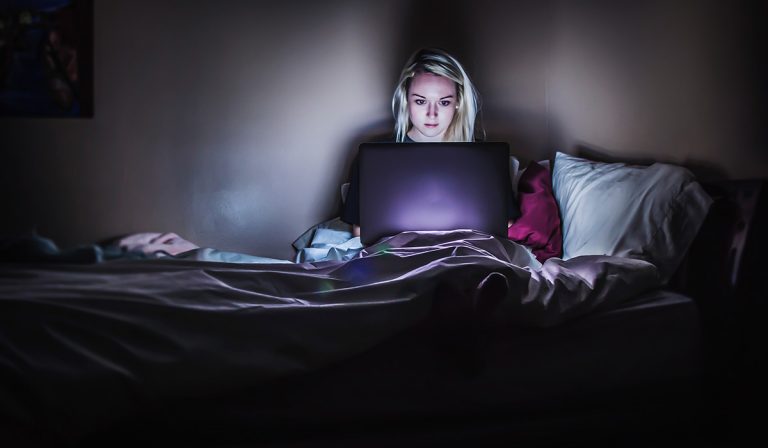 Woman sitting in bed, late at night, working on computer