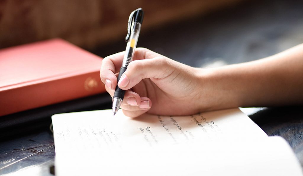 Closeup of woman's hand holding a pen over a journal as she is journaling