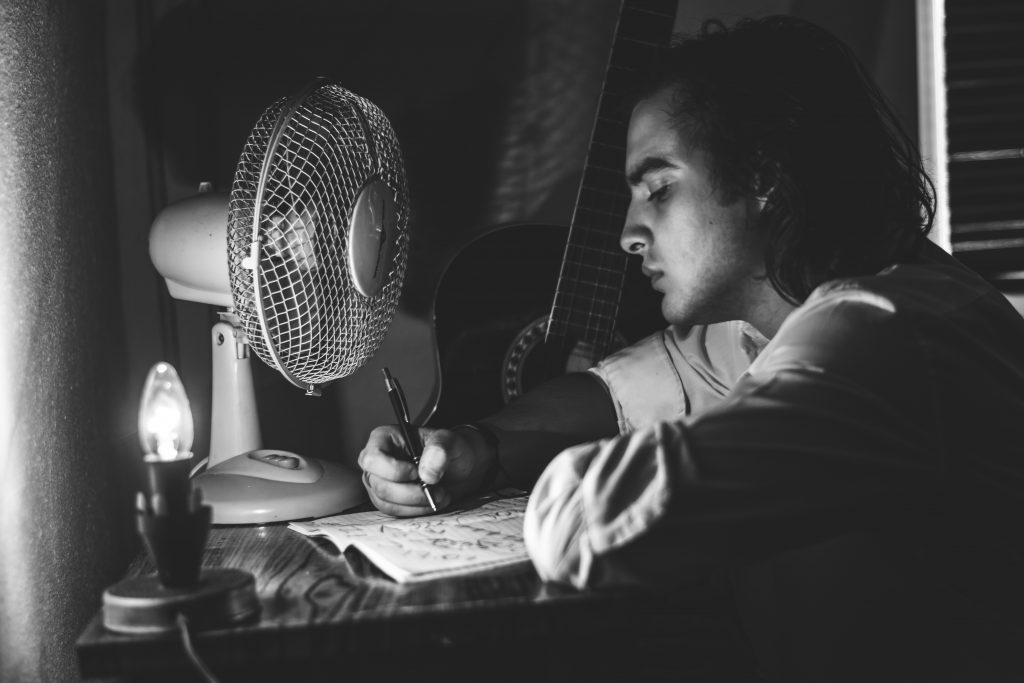 man trying to write website content, fan in front of him, dark room